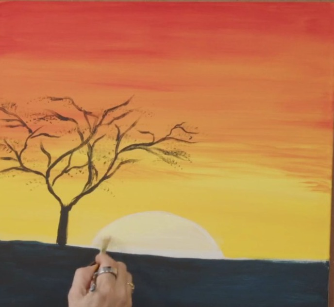 Hand painting a glowing orange sunset with a bare tree silhouette, the first landscape in the course