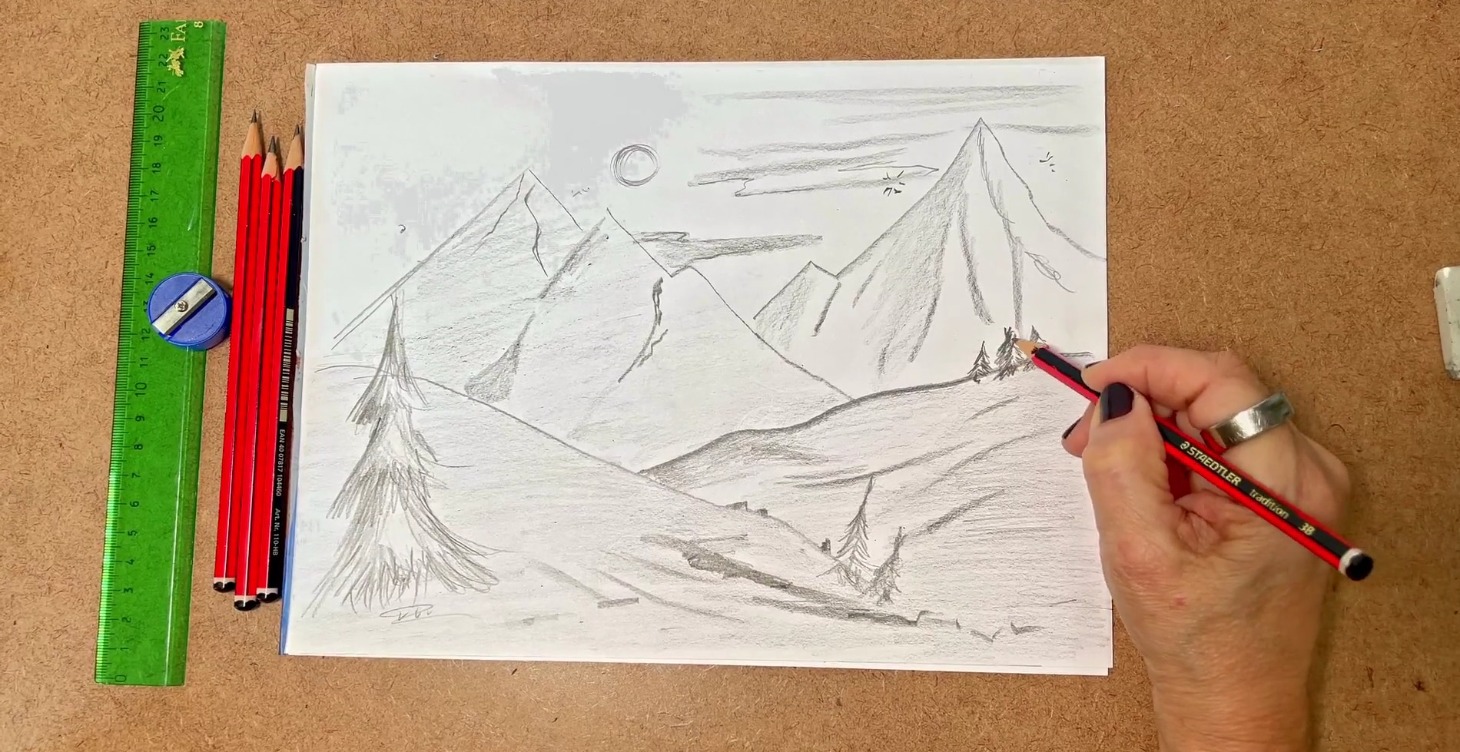 Hand sketching a mountain landscape in pencil with ruler and pencils beside the paper