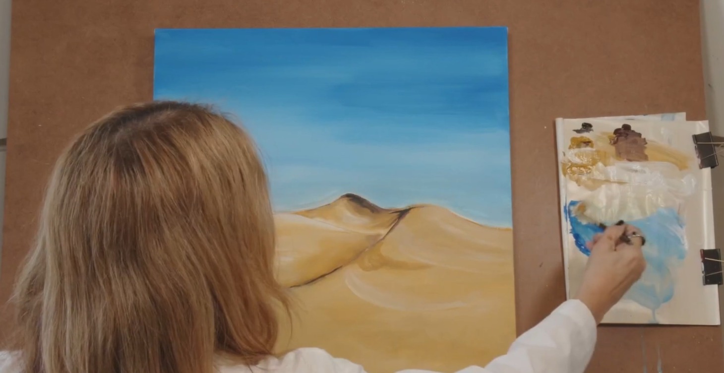 Painting of golden desert dunes under a blue sky in progress